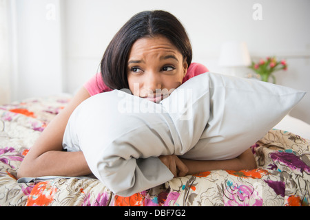 Mixed race woman hugging pillow on bed Stock Photo