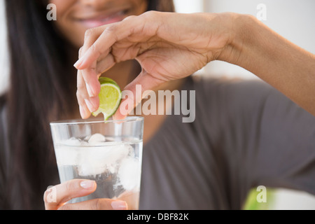 Mixed race woman squeezing lime into drink Stock Photo