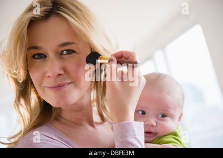 Caucasian mother with baby applying makeup Stock Photo