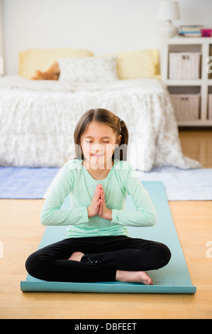 Mixed race girl meditating on yoga mat Stock Photo