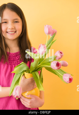 Mixed race girl holding vase of flowers Stock Photo