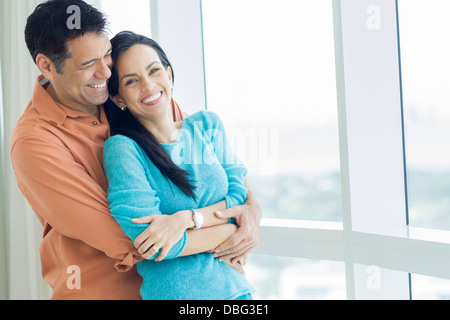 Hispanic couple hugging at window Stock Photo