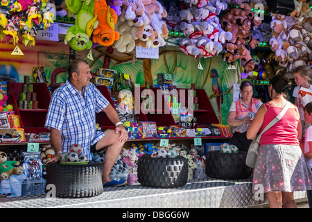 Carnie in stall with ball throwing game at travelling funfair / traveling fun fair Stock Photo