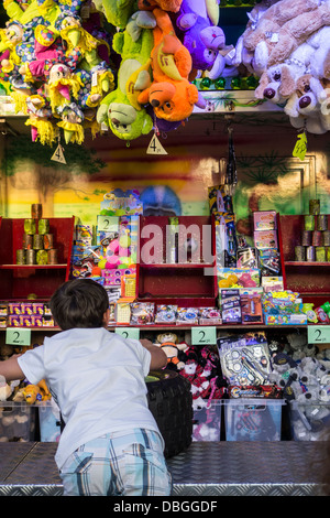 Boy at fun fair aiming at tin cans in booth with ball throwing game at travelling funfair Stock Photo