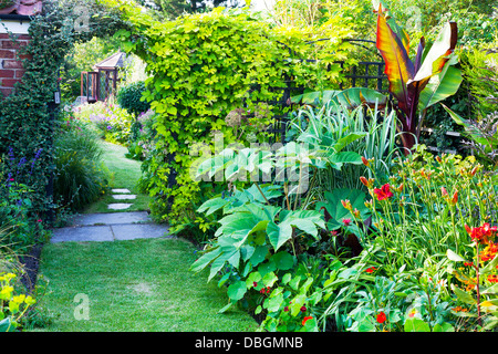 Typical English garden plants flowers planted at side of path leading through arch to summer house Stock Photo