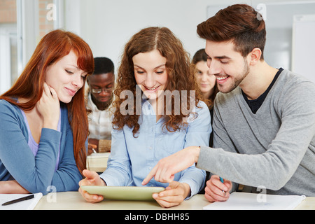 Three happy students learning in class with a tablet PC in classroom Stock Photo