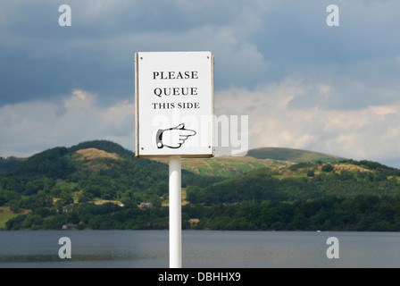 Sign - Please queue this side - with Ullswater in the background, Lake District National Park, Cumbria, England UK Stock Photo