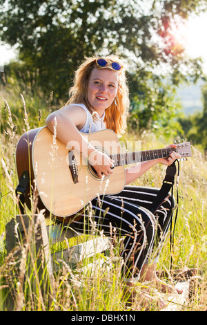 Teenage girl playing guitar in a grassy field. Outdoors. Summer. Stock Photo