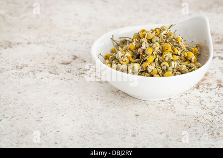 small ceramic bowl of dried chamomile flowers against a ceramic tile background with a copy space Stock Photo