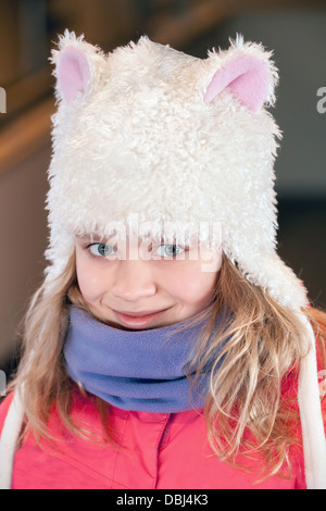 Little blond girl in fun white artificial fur hat. Closeup outdoor portrait Stock Photo