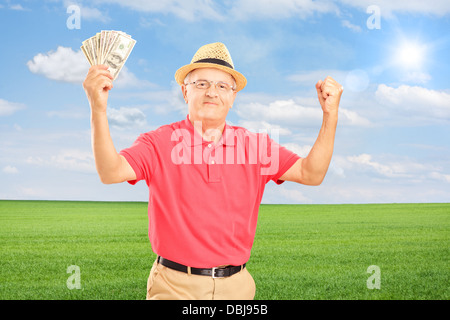 Happy senior man holding money banknotes and gesturing happiness on a field Stock Photo