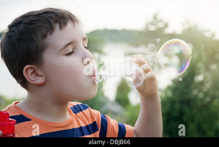 Young boy blowing soap bubbles in summer evening sunlight with green nature background Stock Photo