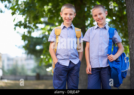 Image of happy twin boys with backpacks standing in summer park Stock Photo