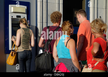 Shoppers waiting in queue to collect money from ATM cash dispenser at cashpoint of bank in shopping street Stock Photo