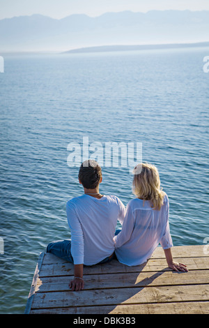 Croatia, Young couple sits on boardwalk, rear view, by the sea Stock Photo