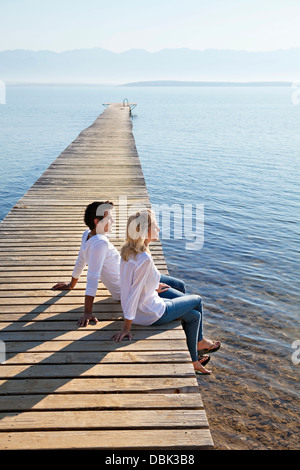 Croatia, Young couple sits on boardwalk, by the sea Stock Photo