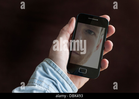 Man holding a mobile phone, reflection of his face on the screen. Landscape. MR. Stock Photo