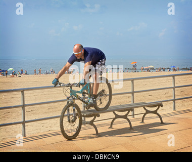 BIcycle stunt. A man riding his bike over a bench on the boardwalk in Brighton Beach Brooklyn, New York Stock Photo