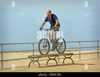 BIcycle stunt. A man riding his bike over a bench on the boardwalk in Brighton Beach Brooklyn, New York      v Stock Photo