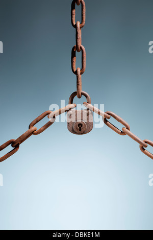 Old rusty lock holding three rusty chains together. Stock Photo