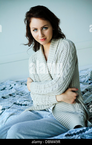 Woman with brown hair sits on bed, crossed arms, Copenhagen, Denmark Stock Photo