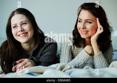 Two young women lying down on bed smiling, Copenhagen, Denmark