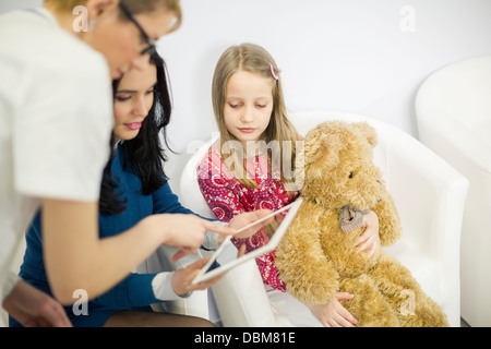 Female doctor and woman looking at digital tablet, girl holding a teddy bear, Osijek, Croatia Stock Photo