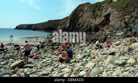 People sitting on the rocky beach at low tide at Caerfai Bay in summer St. Davids Pembrokeshire Wales UK Stock Photo