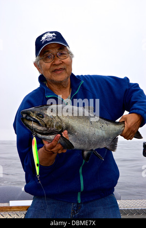 Happy smiling Asian angler holding sport caught chinook salmon trolling spoon lure Swiftsure Bank BC Stock Photo