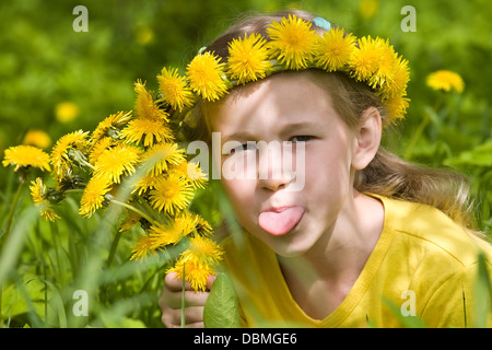 closeup portrait of little girl in dandelion wreath putting out her tongue Stock Photo