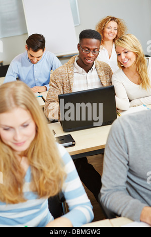 Students studying with laptop computer in class and talking to each other Stock Photo