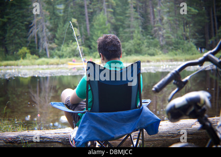 A teenage boy fishing by the lakeside in his camp chair Stock Photo