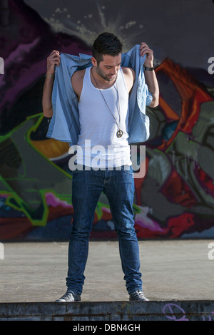 Young man standing in front of graffiti wall, Munich, Bavaria, Germany Stock Photo