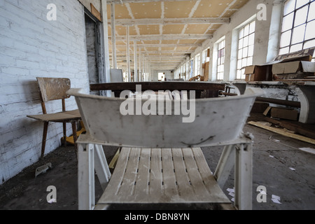 Abandoned factory with broken stuffs on the ground like chairs and wood panels. nobody. Focused on the table and the background. Stock Photo