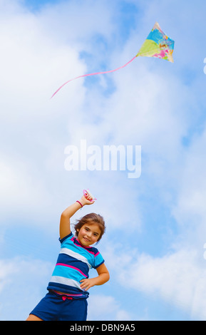 Adorable baby girl play with colorful kite outdoors, nice kid with toy on blue sky background, spending time in daycare Stock Photo