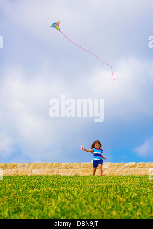 Sweet little girl running with kite on green field, adorable child having fun on backyard, playing game with windy paper toy Stock Photo
