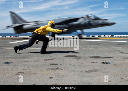A US Navy Aviation Boatswain Mate signals a AV-8B II Harrier fighter jet to launch off the flight deck of the amphibious assault ship USS Wasp July 27, 2013 operating in the Atlantic Ocean. Stock Photo