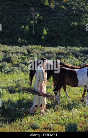 native American Indian girl in traditional costume gathers firewood in horse meadow pasture Stock Photo