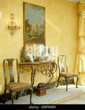 Large painting above marble+metal console table in hall with painted antique chairs and damask wallpaper Stock Photo
