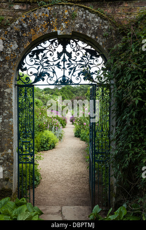 View of the walled garden of Rousham House in summer through the blue ornate wrought-iron gate set in a Cotswold-stone archway, Oxfordshire, England. Stock Photo