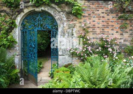 Ornate wrought-iron gate set within a Cotswold stone arch and 17th century brick wall, Rousham House, Oxfordshire, England Stock Photo