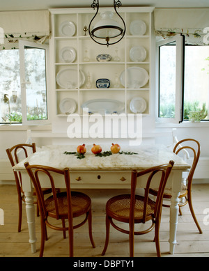 Simple white shelves and painted table with old Bentwood chairs in white coastal dining room with wooden floor Stock Photo