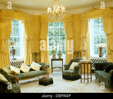 Yellow swagged and tailed silk curtains on tall windows in yellow townhouse drawing room with dark green sofas and cream carpet Stock Photo