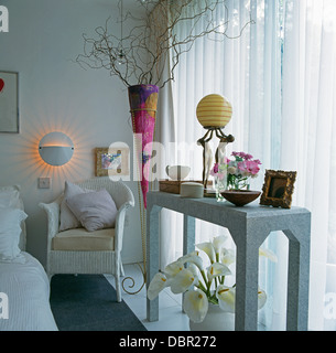 Tall pink conical vase with twisted willow in modern white bedroom with white Lloyd Loom chair and console table Stock Photo