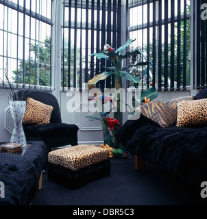 Animal-print cushions on black armchairs and sofa in front of window with black Venetian blind in nineties living room Stock Photo