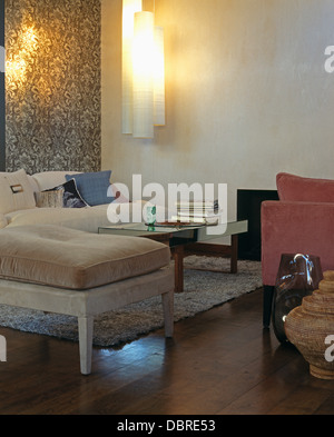 Velour cushions on stool in modern living room with cylindrical wall light and patterned gray wallpaper on one wall Stock Photo