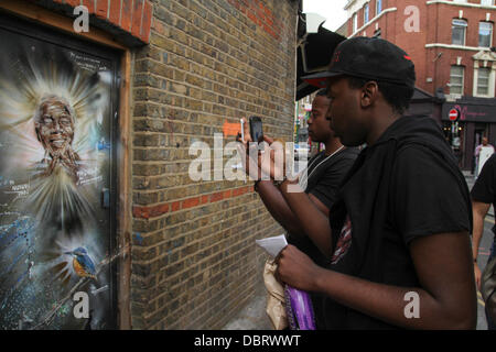 London 3 August 2013.  South African youth seen taking photos of the portrait of 'Madiba' on Brick Lane.  Credit David Mbiyu/Alamy Live News Stock Photo