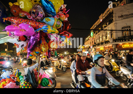 HANOI, Vietnam — Busy traffic on bicycles and scooters at night in Hanoi's Old Quarter. At left a balloon vendor sells his wares. Stock Photo