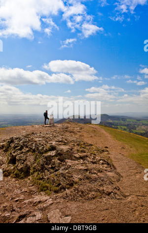 A lone walker rests by the trig point on the summit of Worcestershire Beacon - highest point of the Malvern Hills, England, UK Stock Photo