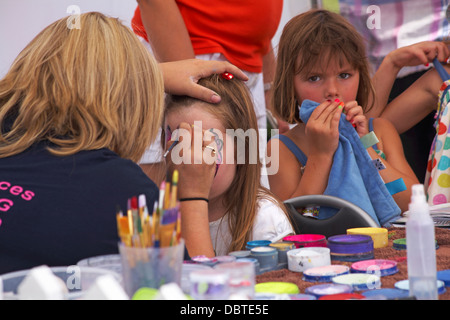 face painting - woman painting pink butterfly design on girl's face Stock Photo